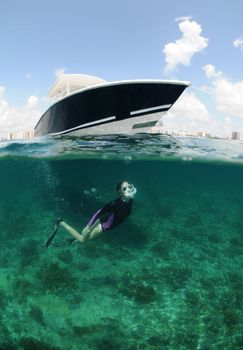 fit young woman snorkeling underwater in ocean with boat in background