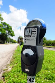 A parking meter on a street with green grass and sky in background