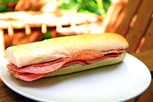 Sub sandwich with salami and lunch meat on a white baguette outdoors