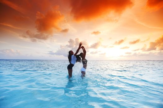 Two happy wimen playing in water on sunset