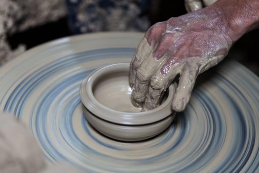 hands on a piece of pottery made of clay on a rotating wheel.