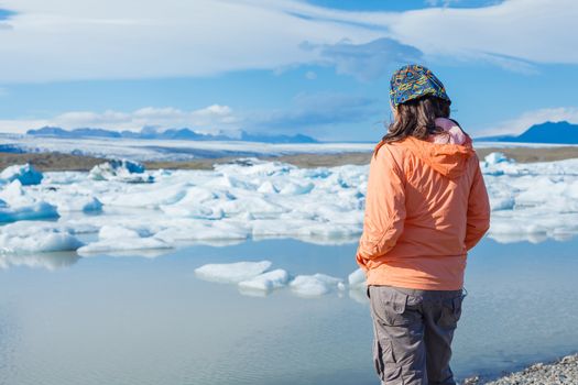 Young woman enjoying the view Jokulsarlon a lake in Iceland where icebergs collapsing from Vatnajokull glacier are floating around.