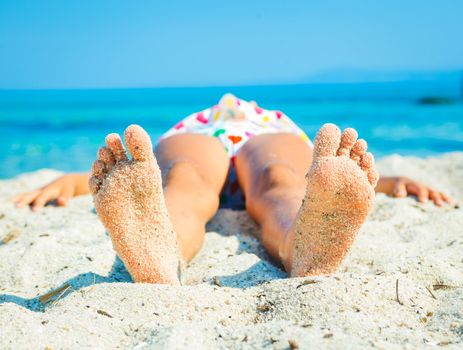 Close-up view of foots by the girl lying on the sand beach.
