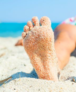 Close-up view of foot by the girl lying on the sand beach. Vertical view