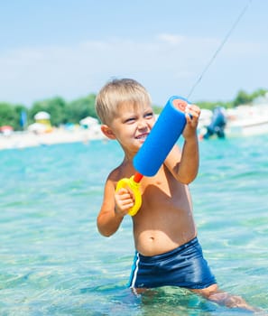 Portrait of young boy swimming and plaing water pistol in the transparent sea