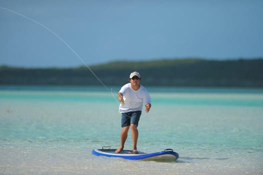 Man in a tropical paradise fishing off his paddleboard

