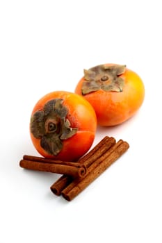 Closeup of persimmons and cinnamon on white background.