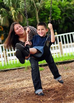 Beautiful mother pushing her son on a swing at a park outdoors