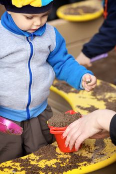 little boy playing in the sandbox with mother