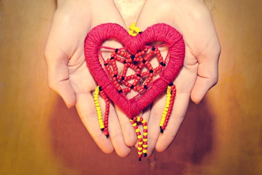 Red heart of colored beads in female hands.