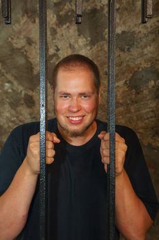 Young man looking from behind the bars