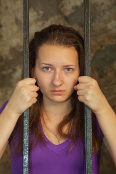 Young woman looking from behind the bars