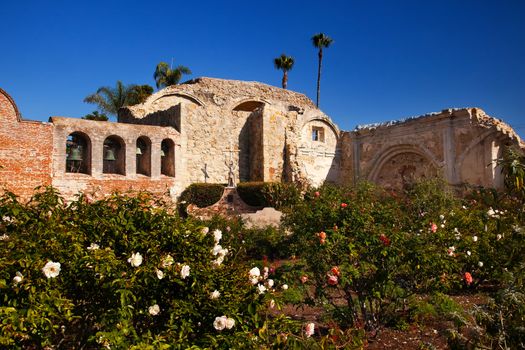 Mission San Juan Capistrano Church Rose Gardens and Ruins in California.  The statue of Father Junipero Serra, who founded the Mission in 1775, and mission bells in the back.  The church was destroyed in 1812 by earthquake.