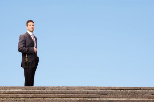 Successful businessman standing on stairs against a blue sky background