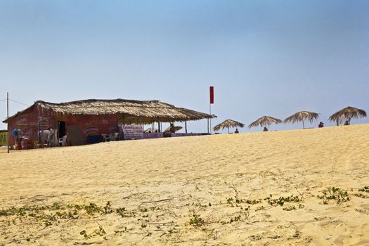 landscape of a sandy beach with refreshment and food shack on a generic beach in Goa India. Dat tripers and holidaymakers basking in the sun