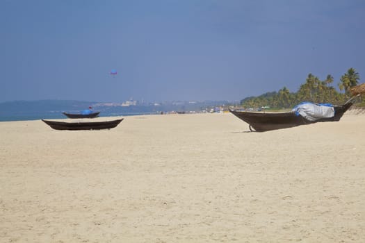 Landscape of secluded beach with white sand, blue sky, sea, surf, para gliders and fishing boats for a backdrop. Generic tropical shot location, Goa India