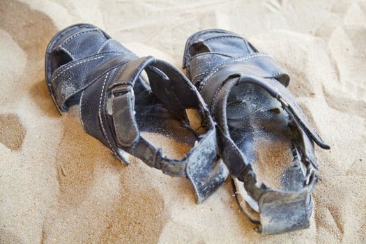 horizontal landscape of a pair of generic old black leather sandals, still fastened left in sand. location of this shot was goa, india