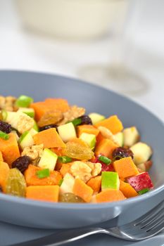 Blue bowl of fresh salad made of cooked sweet potatoes, fresh apples, nuts, raisins and shallots (Selective Focus, Focus one third into the salad)