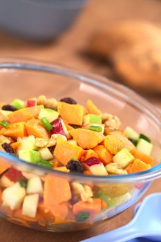 Glass bowl of fresh salad made of cooked sweet potatoes, fresh apples, nuts, raisins and shallots (Selective Focus, Focus one third into the salad)