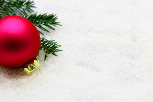 One red Christmas ornament with pine needles on snow