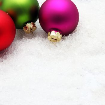 Three red, violet and green Christmas globes in snow, with copy space