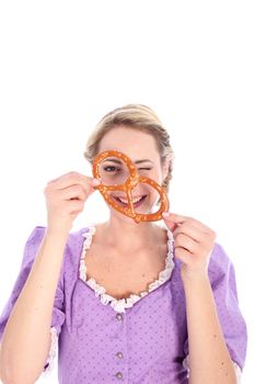Portrait of a smiling blond girl, wearing a dirndl dress and looking through a bretzel