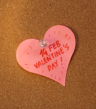 A heart shade sticker is pinned on a cork board and written valentine's day reminder on