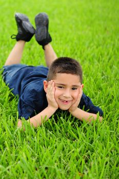 Happy young boy lying in grass with hands on face smiling