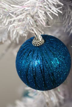 Shiny blue glitter ornament on white christmas tree