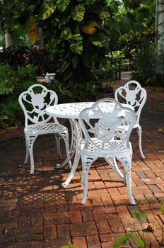 white ornamental garden chairs in a backyard patio with surrounding garden