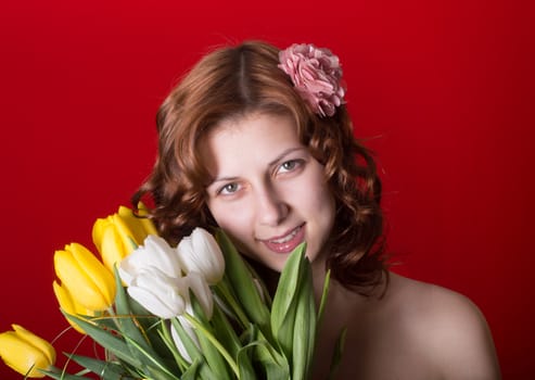 Beautiful green-eyed girl with a bouquet of tulips on red background