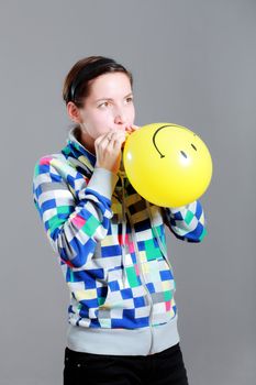 girl inflating a yellow smiley balloon, against grey background