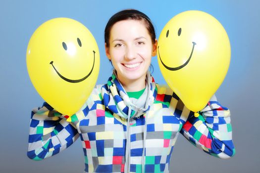 girl with two yellow smiley balloons against blue