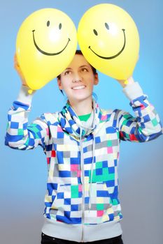 girl with two yellow smiley balloons against blue