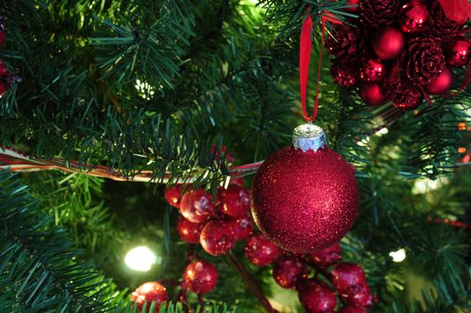 red glitter decoration on christmas tree with ribbon and berries