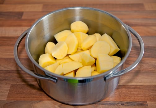 Raw potatoes in steel pan over wooden background