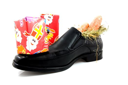 Big black men shoe with carrots and presents for typical Dutch Sinterklaas, over white background