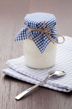 Homemade milk yogurt in glass pot and metal spoon served on linen napkin wooden table
