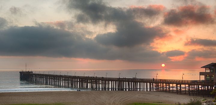Pier at Ventura coast in California as the sun is setting over calm Pacific ocean