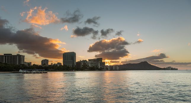 Early morning sunrise at dawn illuminates clouds over Diamond Head and Waikiki Beach area of Oahu in Hawaii