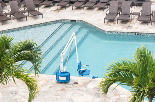 Disabled person pool lift meets ADA standards installed by swimming pool to lower people into water
