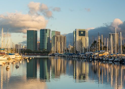 Yachts line harbor at Ala Moana near Waikiki Oahu Hawaii with reflections of office and hotel buildings in still water