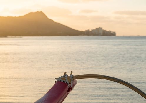 Early morning sunrise at dawn illuminates outrigger of traditional Hawaiian canoe by Diamond Head and Waikiki Beach area of Oahu in Hawaii