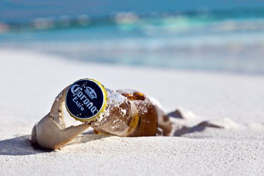 A crab emerges its claw from the sand and opens a bottle of Corona Beer on Maroma Beach in Riviera Cancun, Mexico.