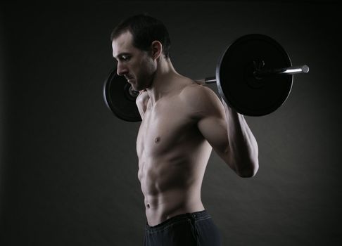 Muscular male athlete is training by lifting the barbell