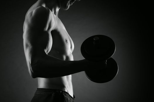 Muscular male athlete is training by lifting dumbbells