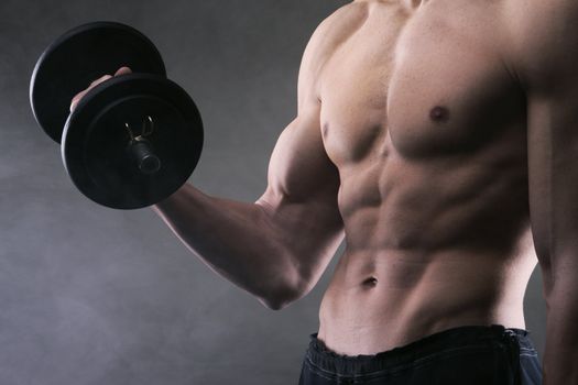 Muscular male athlete is training by lifting dumbbells