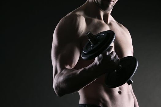 Muscular male athlete is training by lifting dumbbells