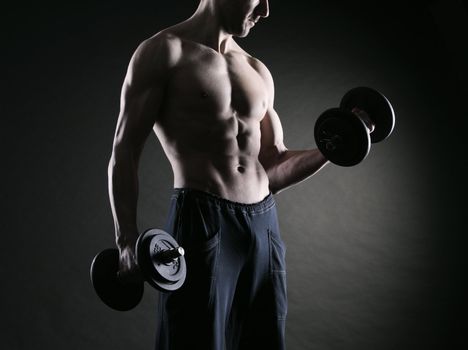 Muscular male athlete is training by lifting dumbbells