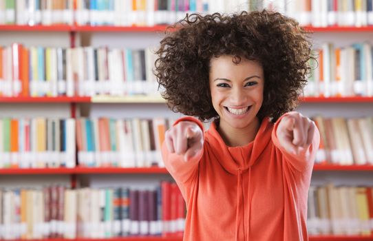 Portrait of beautiful female student in library pointing at viewer